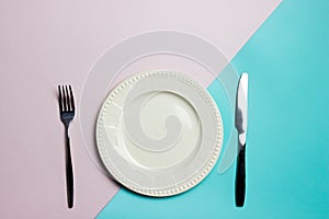A white plate with fork and knife on pink and blue background.