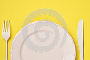 White plate, fork and spoon on a trendy yellow background. Time to eat. Diet concept