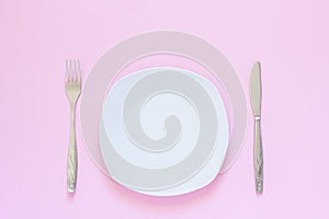 White plate and fork, table-knife on pink background