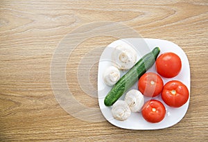 White plate with fresh tomatoes, mushrooms and cucumbers on a wooden table