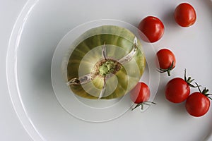 White Plate with fresh vegetables on wooden table. Two cucumbers, red cherry tomatoes, green cracked tomato with vertical splits,