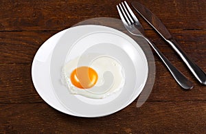 White plate with fried egg on wooden