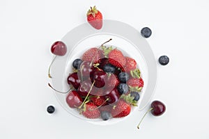 A white plate with juicy cherries, strawberries and blueberries, decorated with mint, stands in the center on a white