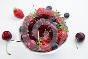 A white plate with juicy cherries, strawberries and blueberries, decorated with mint, stands on a white background