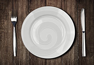 White plate, knife and fork on old wooden table