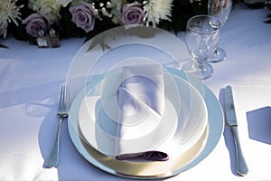 White plate with light violet napkin, clearwine glass and florals - lilis, roses and chrysanthemum. Wedding reception table