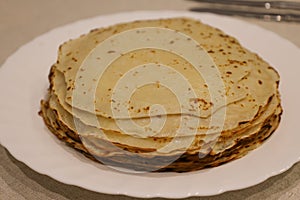 White plate on linen tablecloth with fresh pancakes according to Russian recipe