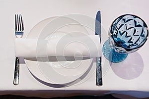 white plate with napkin and cutlery, beautiful blue glass wine glass on table.