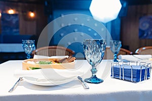 white plate with napkin and cutlery, beautiful blue glass wine glass on table.