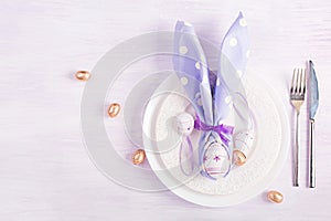 White plate with a napkin folded in the shape of a rabbit, Easter and chocolate eggs on a pink background.