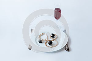 White plate with necklace and black crystals on it, fork, knife and glass of champagne on a white background