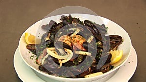 White plate with prepared mussels in white wine with lemon, prawns and basil. Fresh restaurant dish.