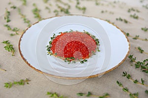 White plate of red caviar decorated with sprigs of thyme