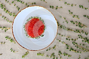 White plate of red caviar decorated with sprigs of thyme