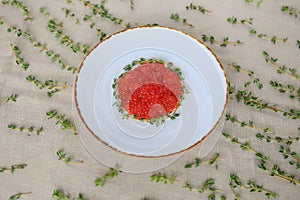 White plate of red caviar decorated with sprigs of thyme