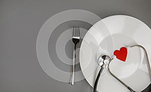 White plate with red heart and stethoscope and knife and fork on grey background with copy space,health care and diet concept