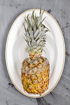 White Plate with Ripe Whole Pineapple on Grey Concrete Background