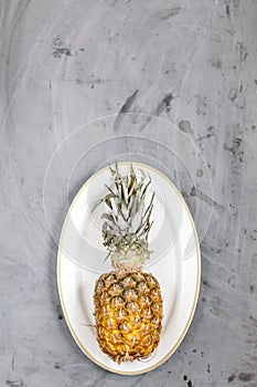 White Plate with Ripe Whole Pineapple on Grey Concrete Background. Copyspace