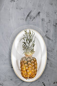 White Plate with Ripe Whole Pineapple on Grey Concrete Background. Copyspace