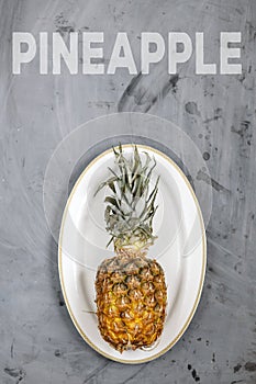 White Plate with Ripe Whole Pineapple on Grey Concrete Background. Word Pineapple