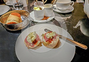 White plate with scone. Jam and cream applied with a knife