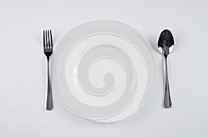 A white plate with silver fork and spoon isolated on white background with copy space. Dinner place setting. Table Setting.