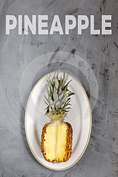 White Plate with Sliced Whole Pineapple on Grey Concrete Background. Word Pineapple