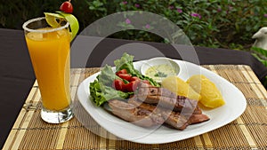 White plate with smoked pork meat accompanied by fried yucca and lettuce and tomato salad on wooden table