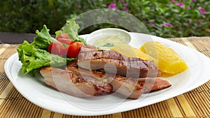 White plate with smoked pork meat accompanied by fried yucca and lettuce and tomato salad on wooden table