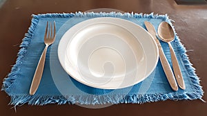 White plate with spoon, fork, knife on the blue napery
