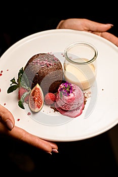 white plate with tasty chocolate cake with ice and jar of cream in female hands