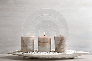 White plate with three burning candles and rocks