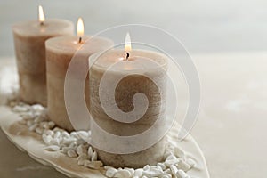 White plate with three burning candles and rocks on table