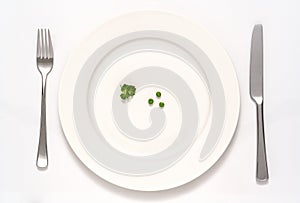 White plate with three peas and some parsely with knife and fork isolated on a white background