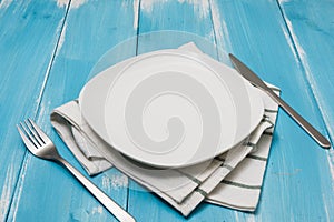 White Plate with utensils and dish towel on blue wooden background with perspective
