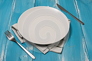 White Plate with utensils and dish towel on blue wooden background with perspective