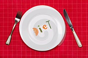 White plate with word diet made of pieces of vegetables on red tablecloth background. Fork and knife near it. Flat lay. Top view.