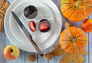 White plates with fresh juicy ripe plums, pumpkins, walnuts, apple and nectarine with autumn leaves on blue background