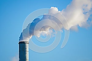 A white plume of steam rising from a cooling tower against a clear blue sky.