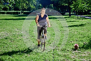 White plus size woman riding bicycle in public park on sunny summer day.