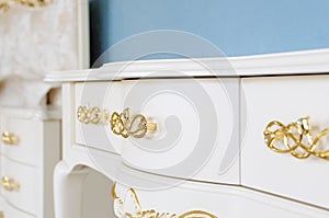 White polished chest of drawers with golden handles. Luxurious chest of drawers in a classic style