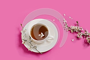 White porcelain cup with black tea. Branches of a blossoming apple tree lie on a bright pink background. Spring concept