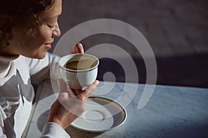 A white porcelain cup with coffee drink in hands of a smiling woman telling fortunes on coffee grounds. People. Leisure