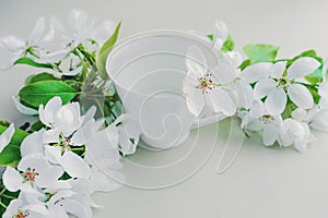 White porcelain cup with green tea and a fresh white pear tree flower in a lush bouquet of blooming white flowers and green bright