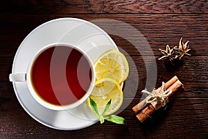 White porcelain cup of tea with cinnamon sticks, lemon, mint leaves and tea strainer on wooden rustic table.