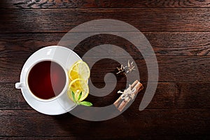 White porcelain cup of tea with cinnamon sticks, lemon, mint leaves and tea strainer on wooden rustic table.