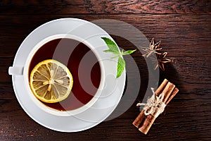 White porcelain cup of tea with cinnamon sticks, lemon, mint leaves and tea strainer on wooden rustic table.