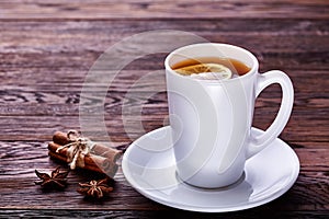 White porcelain cup of tea with cinnamon sticks, lemon, mint leaves and tea strainer on wooden rustic table.