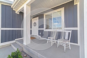 White porch chairs against window and front door of home with gray exterior wall