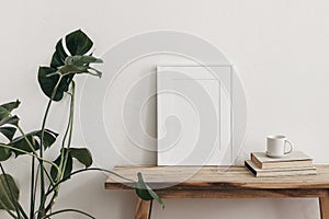 White portrait frame mockups on vintage bench, table. Cup of coffee on pile of books and monstera potted plant. White photo